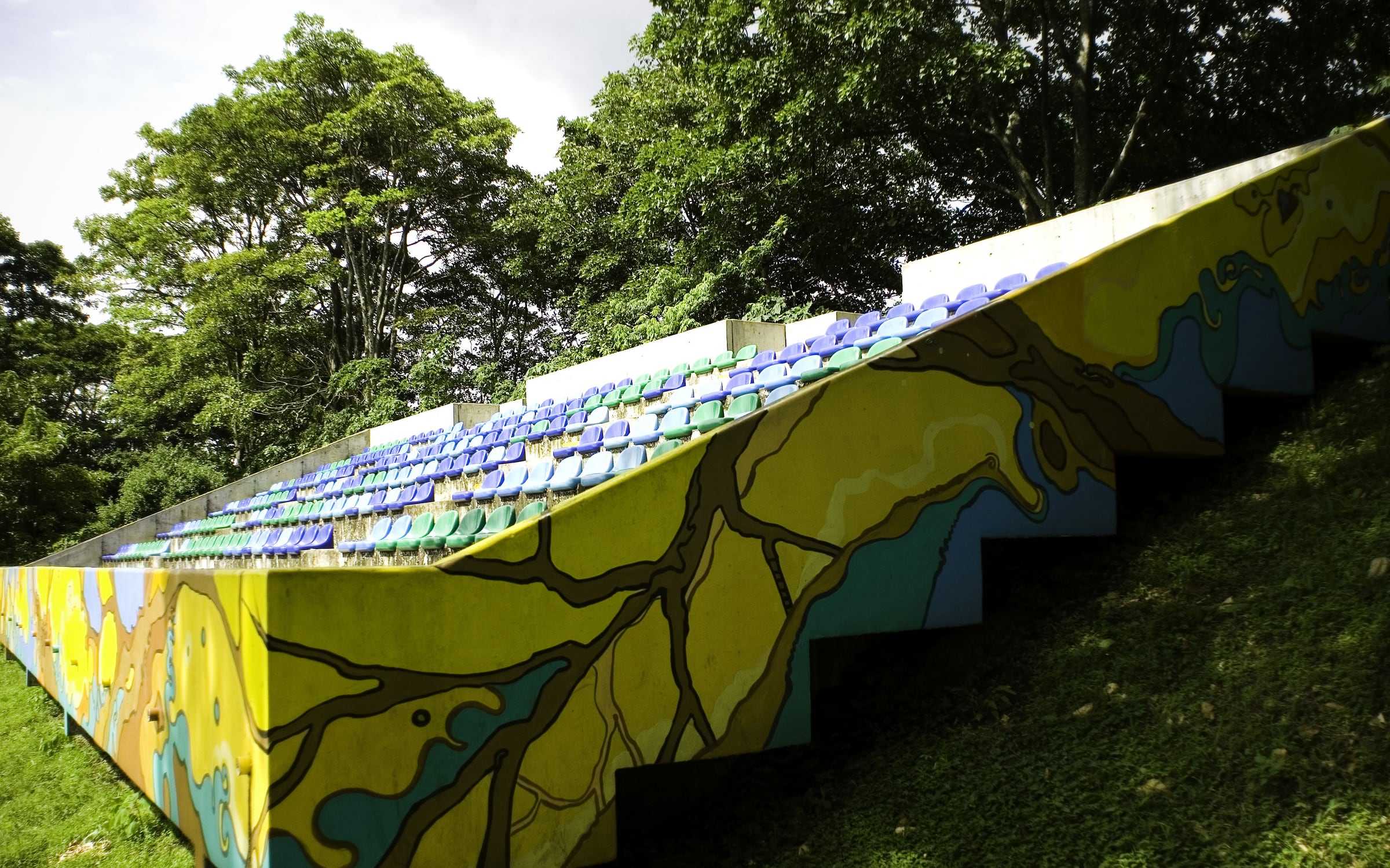 Gradería del Estadio Ecológico de la UCR con un mural de colores y butacas azules