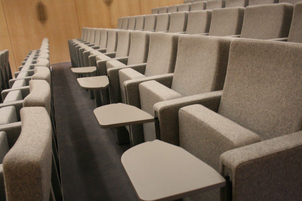 Fila de butacas Rubick en un auditorio con las palas de escritura abiertas junto a cada asiento