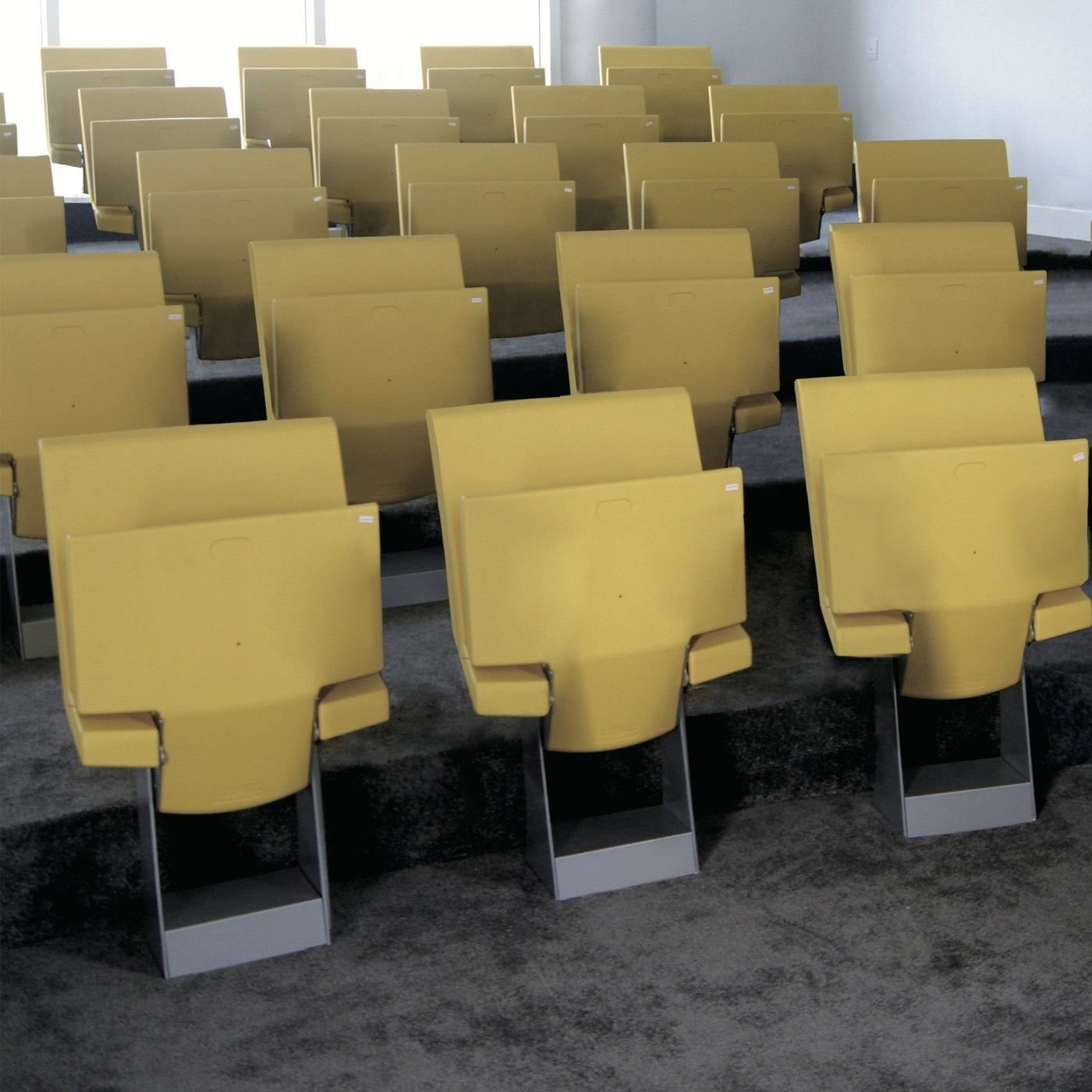Filas de butacas Sporta amarillas con el asiento plegado, instaladas sobre gradas en una sala con alfombra gris